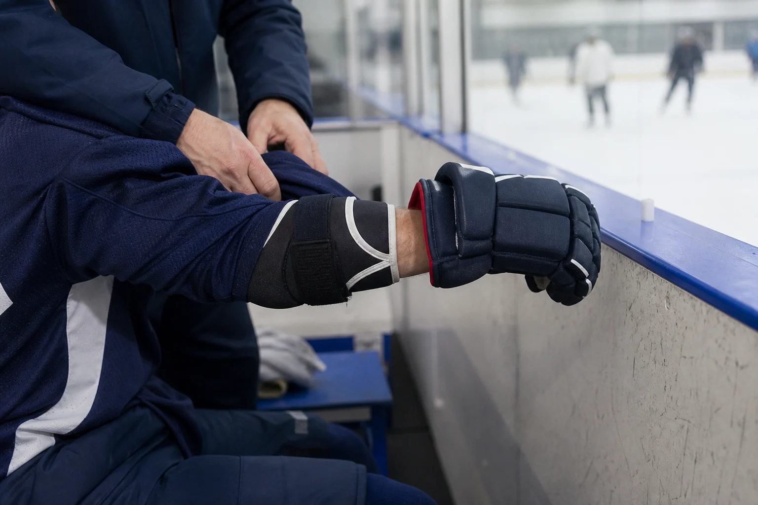 Hockey glove cuff and elbow pad overlap checked at the rink bench